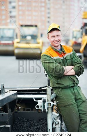 Trabajador operando la máquina pavimentadora de asfalto durante la construcción de carreteras y obras de reparación