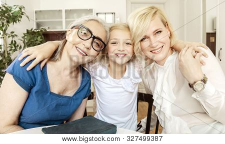 Portrait Of Cheerful Young Blonde Woman With Her Dearest Mother And Daughter In A Living Room