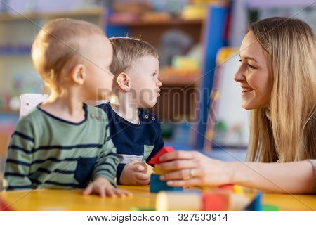 Nursery Teacher With Cute Little Children In Kindergarten Or Creche