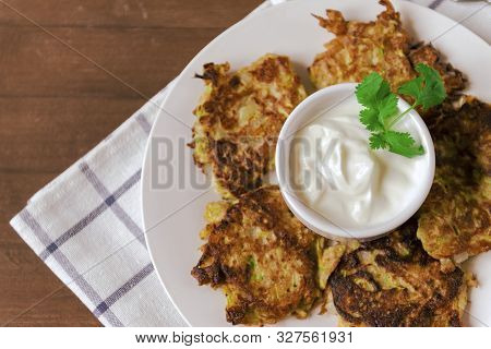 Plate Of Zucchini Fritters With Sour Cream And Greens On Poltice Wooden Background, Top View,  Copy 