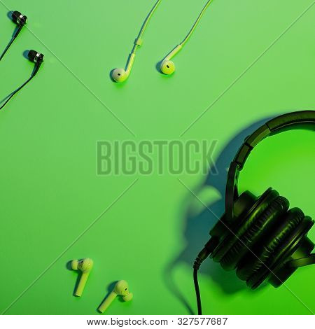 Headphones Of Different Types Flat Lay On Green Color Background, Copy Space. Black In Ear Headphone