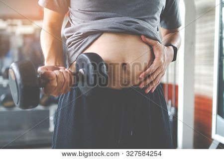 Overweight Fatty Belly Of Man And Holding A Dumbbell. Man Diet Lifestyle Concept To Reduce Belly And