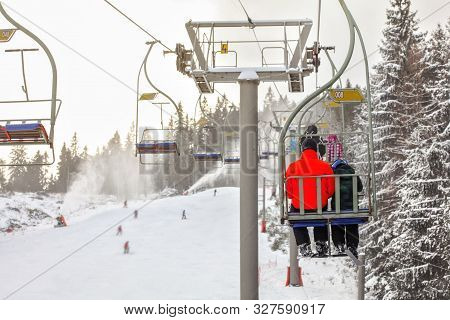View From Chairlift Over Ski Piste, Skier In Bright Red Jacket Seating In Front, More Blurred People