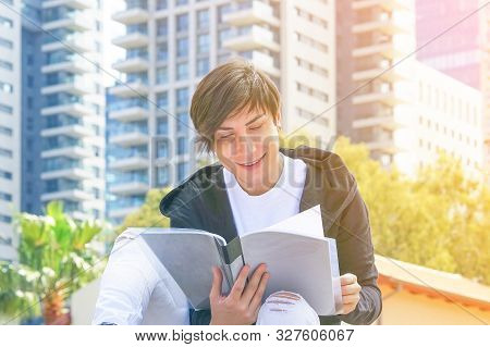 The Student Man Teaches Assignments While Sitting On The Street. Gay Brunet Is Reading The Folder Wi
