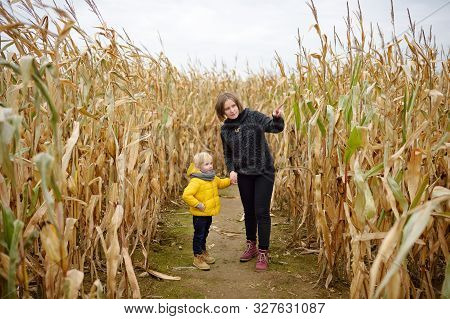 Little Boy With Young Mother Having Fun On Pumpkin Fair At Autumn. Person Walking Among The Dried Co