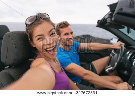 Selfie car travel couple having fun on summer road trip vacation driving to holidays. Asian woman and man excited taking self-portrait photo with mobile phone.