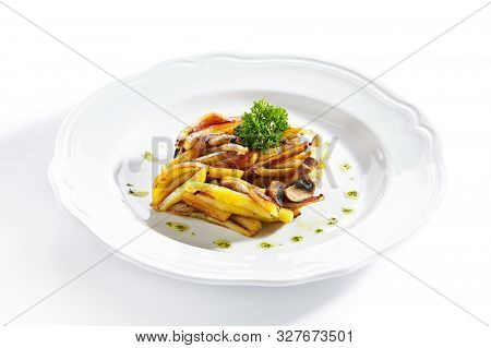 Fried potatoes with mushrooms on a restaurant plate isolated on white background close up. Healthy vegetarian menu with diced backed potato, champignons and greens on flat dish closeup