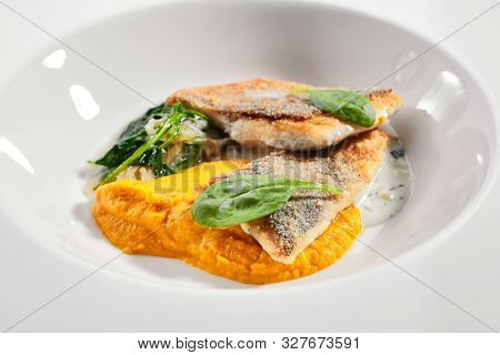 Cod fillet with pumpkin puree and spinach closeup. Seafood restaurant menu item. Delicious healthy food. Exquisite dish isolated on white background. Gourmet meal, tasty lunch close up