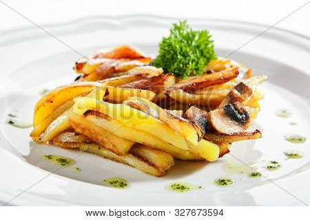 Fried potatoes with mushrooms on a restaurant plate isolated on white background close up. Healthy vegetarian menu with diced backed potato, champignons and greens on flat dish closeup