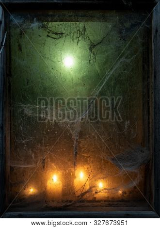 Eerie light of candles in an old window with a cobweb. Halloween background with copy space for text