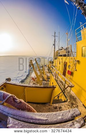  The excursion to the arctic tourist cruise on the sea icebound. Dim polar sun in Lapland. The strip of ice crumb spreads behind the icebreaker. The concept of active and extreme tourism
