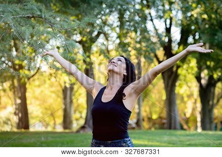 Happt brunette woman raising his arms in a park