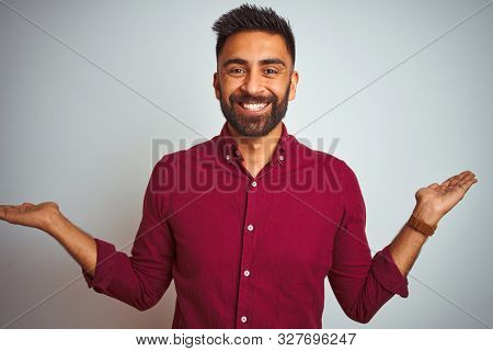 Young indian man wearing red elegant shirt standing over isolated grey background smiling showing both hands open palms, presenting and advertising comparison and balance