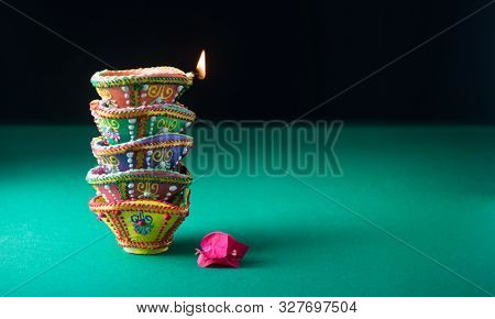 Brightly handpainted traditional Indian earthen lamps stacked on bright green background. Beautiful Diwali background with diyas and flower with clear space for headline.