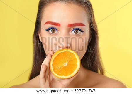 Young woman with dyed eyebrows and half of orange on color background