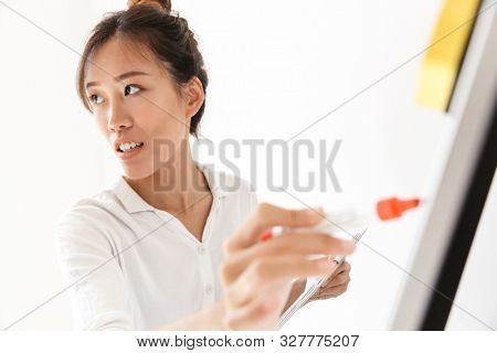 Attractive confident asian businesswoman presenting new project at the blankboard isolated over white background