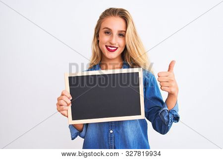 Young beautiful teacher woman holding blackboard standing over isolated white background happy with big smile doing ok sign, thumb up with fingers, excellent sign