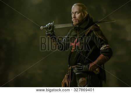 Portrait of a medieval knight in armour and with a sword over black background. Knight Templar. Historical reenactment.