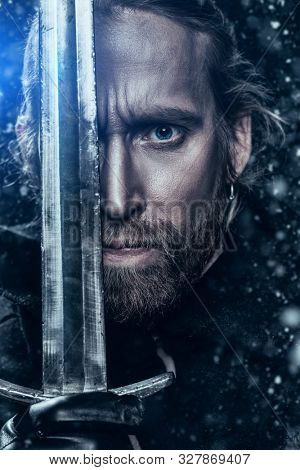 Close-up portrait of a medieval knight in armour and with a sword over black background. Historical reenactment.