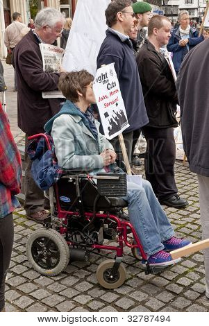 Un manifestante en una silla de ruedas tiene un cartel de Anti-cuts en la yarda de Catedral de Exeter como parte de la mayo
