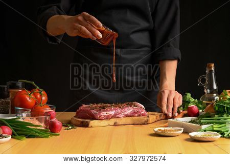 Chef Cooks Pork Steak. Pouring Sauce, Marinade On A Background W