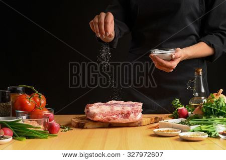Chef Cooks Pork Ribs. Sprinkling With Salt On A Background With