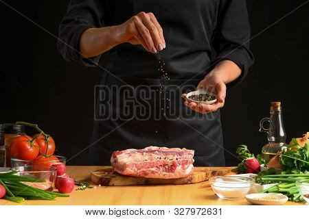 Chef Cooks Pork Ribs. Sprinkling With Pepper On A Background Wit