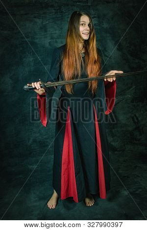 Full Length Portrait Of Young Long Haired Woman Wearing Medieval Costume. Standing Pose Holding A Sw