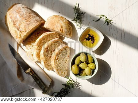 Sliced Organic Bread Ciabatta With Vintage Linen Napkin And Bowl Of Olive Oil, Olives, Rosemary On W
