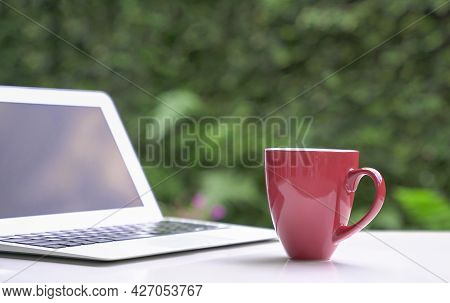 Good Morning With Coffee In Red Cup With Computer Laptop, Green Garden Bokeh Background. Copy Space.