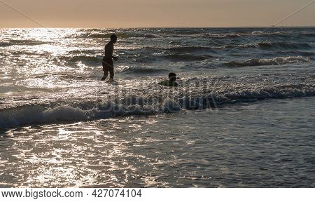 Sabaudia, Italy _ July 10, 2021, Silhouettes Of Two People At Sunset Against The Background Of Waves