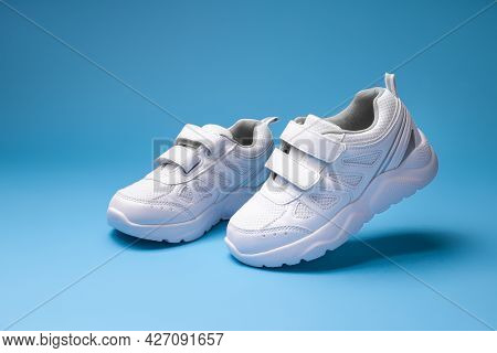 Two White Unisex Running Shoes Simulate Walking And Flying In The Air, Isolated On A Blue Background