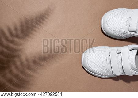 Flat Lay Two White Child Sneakers With Velcro Fasteners With Fern Or Palm Tree Shadows Isolated On A