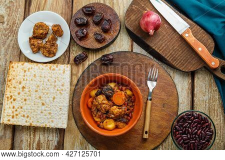 Jewish Dish Chelnt With Meat On The Table In A Plate Near Ingredients And Matzo. Horizontal Photo