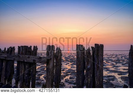 View Of The Wadden Sea During Sunset, At Low Tide. A Colorful Dramatic Sky. Wooden Posts As A Silhou