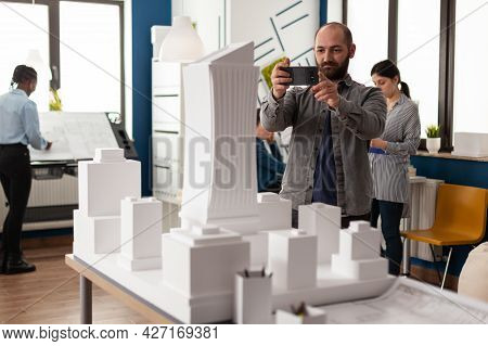 Architect Profession Man Looking At Maquette Layout Using Smartphone To Design Building Model Plan M