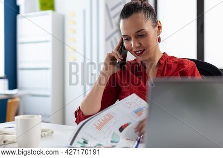 Smiling Entrepreneur Having A Conversation During Phone Call With Colleagues, Checking Finance Chart