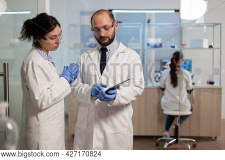 Chemist Nurse Explainig To Doctor Vaccine Development In Modern Equipped Laboratory Pointing On Tabl
