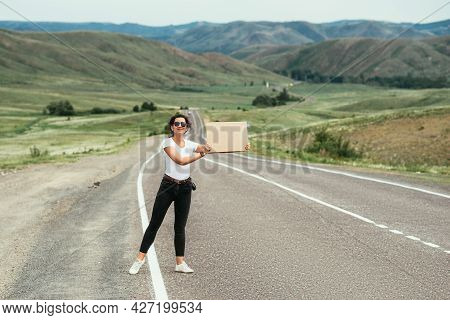 A Young Attractive Woman Hitchhiking On An Empty Road. Hitchhiking Girl. Attractive Young Woman Stan