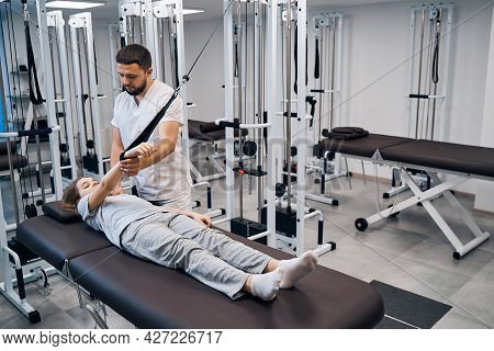 Physiotherapist Treats Girl In Rehabilitation Center On Elastic Machines. Chiropractor Treatments