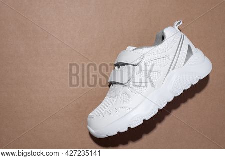 Macro Flat Lay One White Childrens Sneakers With Velcro Fasteners On A Brown Craft Paper Background 