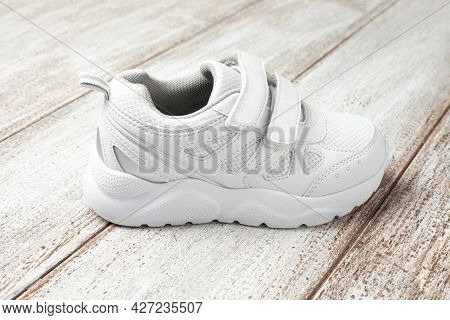 A White Sneaker On A Light Background. One Childrens Leather With Fabric Sports Sneaker With Velcro 