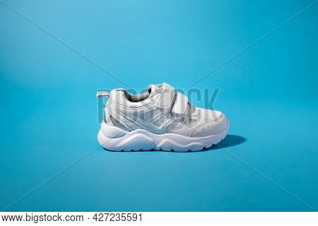 Side View Of One New White Child Sneaker With Velcro Fasteners For Comfortable Footwear On An Insula
