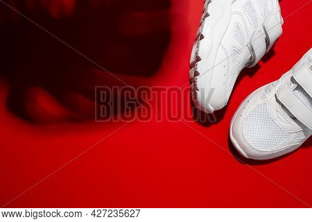 Top View Two White Unisex Sneakers With Hard Shadows From The Monstera Leaf Isolated On A Red Vivid 