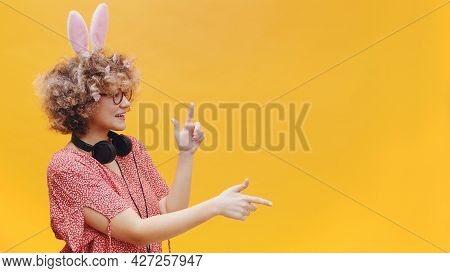 Attractive Young Girl Wearing Cute Bunny Ears And Spectacles In A Joyful Mood. Headphones Around Her