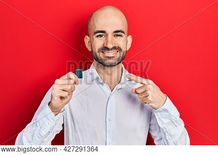 Young bald man holding sdxc card smiling happy pointing with hand and finger 