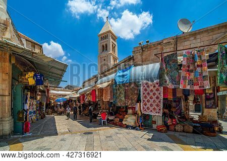 JERUSALEM, ISRAEL - JULY 16, 2018: View of narrow street with traditional  souvenir and carpet shops in Muristan - christian quarter in Old City of Jerusalem, popular place with tourists and pilgrims.
