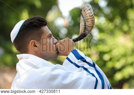 Jewish Man In Kippah And Tallit Blowing Shofar Outdoors. Rosh Hashanah Celebration