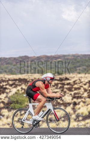 Triathlon time trial competition triathlete man cyclist riding road bike in Hawaii race cycling uphill in tough race in volcanic landscape. Fitness active lifestyle.