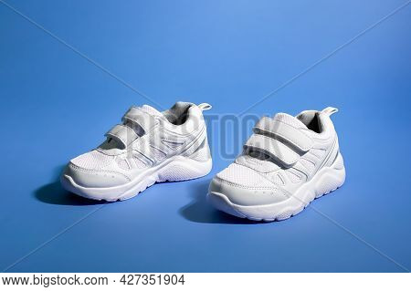 Side View Of Two White Childrens Sneakers With Velcro Fasteners On A Purple Paper Background With Ha